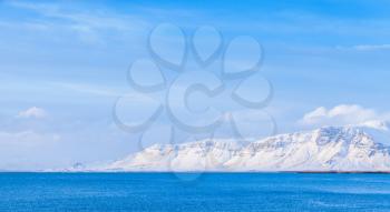 Icelandic coastal landscape, snowy mountains on horizon under blue sky. Reykjavik, Iceland