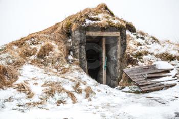 Old cellar with broken door covered with snow. Iceland