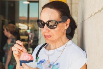 Young adult European woman eats pink ice cream, close-up outdoor portrait 