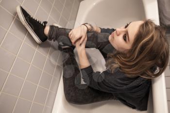 Sad dressed teenage girl sitting in empty bath. Depression mood concept. Vintage tonal correction photo filter