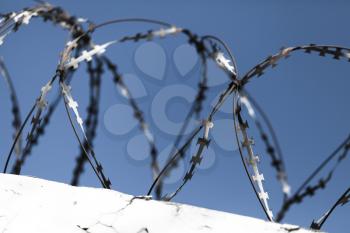 Barbed wire on top of white wall under blue sky background, close-up photo with selective focus