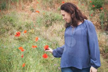 Young adult European woman walks on a summer meadow with flowering poppies. Outdoor portrait