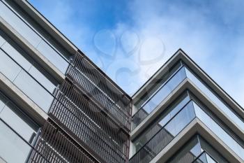 Abstract fragment of modern architecture, walls made of glass and concrete over blue cloudy sky background