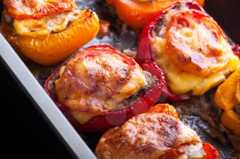 Bell peppers stuffed with chopped meat, cheese and tomato on black baking pan