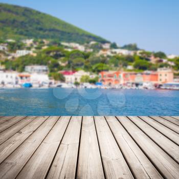 Empty wooden pier perspective with blurred bright coastal town landscape on a background