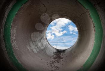 Dark interior of an empty round concrete tunnel with the sky at the and