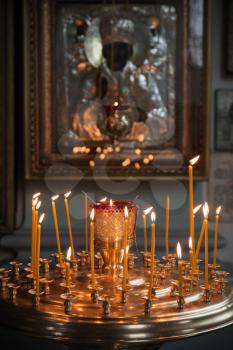 Candles are lit in a dark Orthodox Church above ancient icon