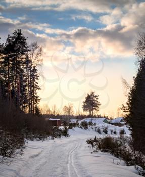 Snowy road in cold winter village under evening cloudy sky. Karelia, Russia