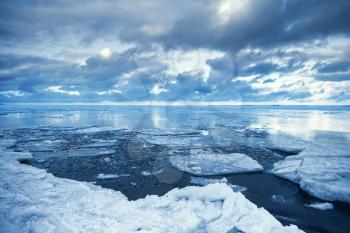 Winter coastal landscape with floating ice fragments on still cold blue water. Gulf of Finland, Russia