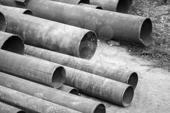 Rusted industrial steel pipes lay on the ground, monochrome photo