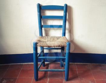Old blue wooden chair with wicker seat stands in empty interior, white wall and red floor tiling. Vintage style. Photo with toned filter effect