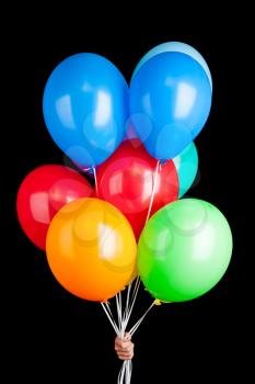 Hand holding group of colorful balloons on ribbons isolated on black background
