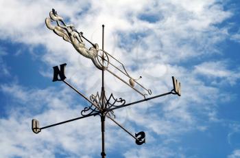 Weather vane against a cloudy blue sky
