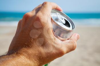 Aluminum can of beer in a male hand with beach and sea on background