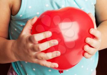 Caucasian baby girl holds red heart shaped balloon in her hands