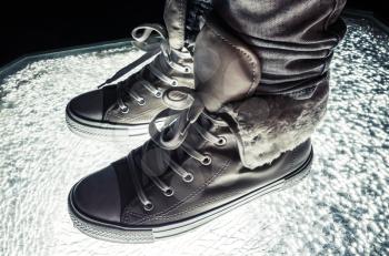 Warm sneakers, sporty shoes standing on cracked glass, cold tonal correction, retro style dark contrast photo filter
