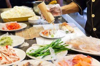 Preparing of traditional Japanese sushi rolls with salmon, cook adds sauce on plate. Selective focus