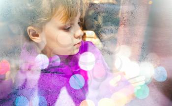 Little blond girl beyond frozen shop window glass with colorful blurred lights