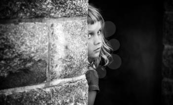 Little blond girl looks out from behind the gray stone wall