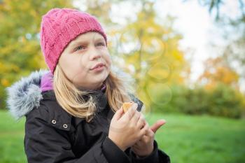 little beautiful blond girl eating cake and thinking about something. Outdoor portrait.