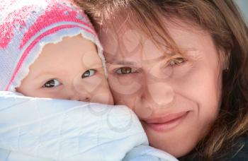 Young European woman holds her sleepy baby in blanket. Outdoor closeup portrait