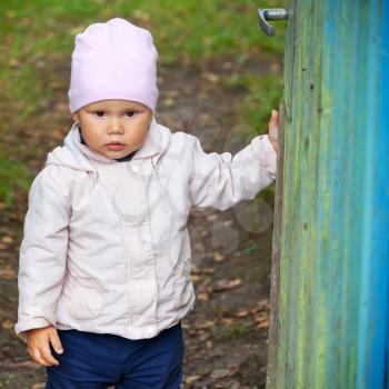 Brown eyed baby girl in pink hat opens old green wooden wicket