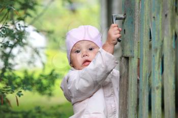 Brown eyed baby girl in pink plays with old green wooden wicket