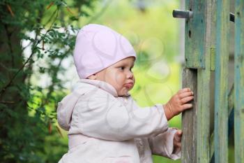 Baby girl in pink hat plays with old green wooden wicket