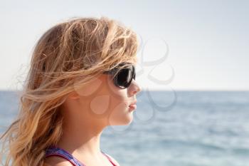 Little blond girl profile portrait with sunglasses on the summer sea coast