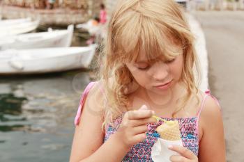 Little smiling blond girl eats ice cream. Outdoor summer portrait
