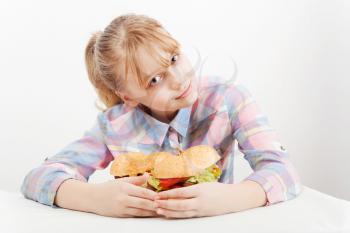 Little smiling blond girl with big homemade hamburgers on plate