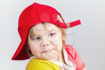 Studio portrait of funny smiling baby girl in red baseball cap over gray wall background