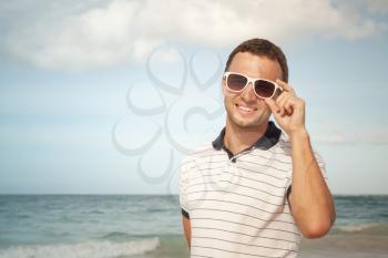Outdoor portrait of young smiling Caucasian man in white sunglasses on summer ocean coast