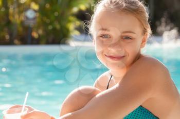Smiling little blond girl with cocktail in the swimming pool