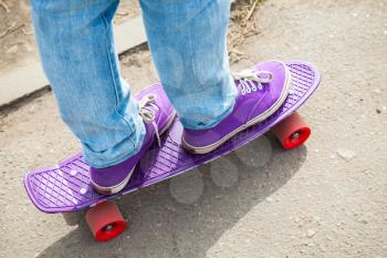 Riding skateboarder feet in a blue jeans and purple gumshoes, selective focus with shallow DOF