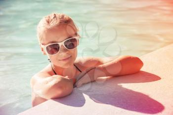Beautiful little blond girl with sunglasses in outdoor pool, closeup summer portrait, colorful  toned photo, old style filter effect