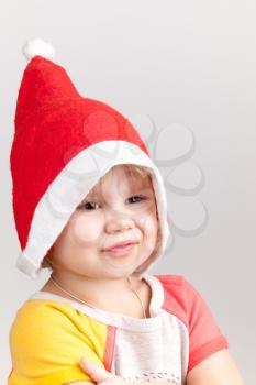 Cute smiling Caucasian little girl in red Santa hat on gray background, closeup studio portrait