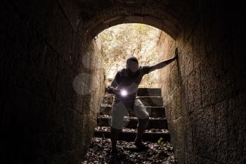 Young man with a flashlight enters the stone tunnel and looks in the dark, warm tonal correction photo filter effect