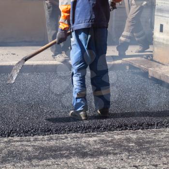Urban road under construction, asphalting in progress, worker with a shovel in blue uniform