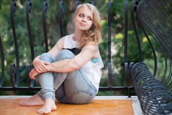 Beautiful smiling blond Caucasian teenage girl sits on balcony, outdoor summer portrait