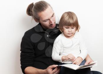 Young man reading book with little Caucasian girl over white wall background, studio shoot
