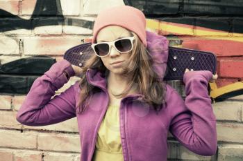 Teenage girl holds skateboard, urban brick wall with graffiti on a background. Vintage tonal correction, old style filter effect