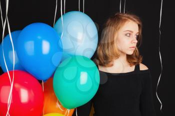 Portrait of beautiful teenage blond girl with colorful balloons over black background