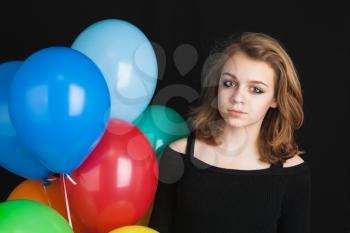 Studio portrait of beautiful teenage blond girl with colorful balloons over black background