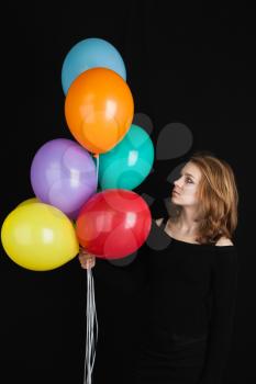 Studio portrait of beautiful teenage Caucasian blond girl with colorful balloons over black background