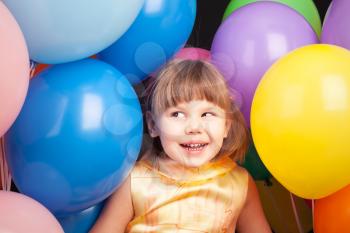 Studio portrait of laughing little Caucasian blond girl with colorful balloons