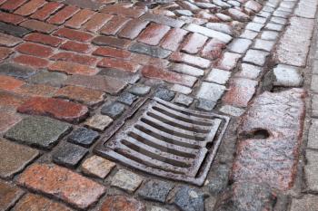 Wet drainage cover on stone pavement of urban road