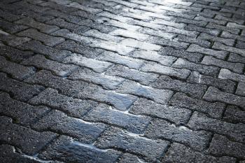 Shining wet cobblestone pavement, abstract urban road background 