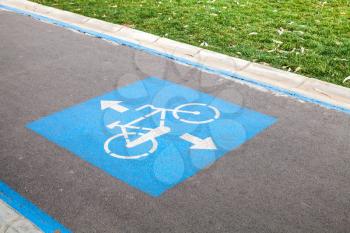 Bicycle lane. Blue and white road marking over urban asphalt road and green grass 