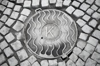 Round hatch in urban stone pavement with big K letter 